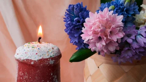 Burning candle made in the shape of Easter cake next to hyacinths Stock Footage 104763047