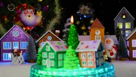 A burning candle surrounded by Christmas trees and colorful houses rotates Stock Footage 295758596