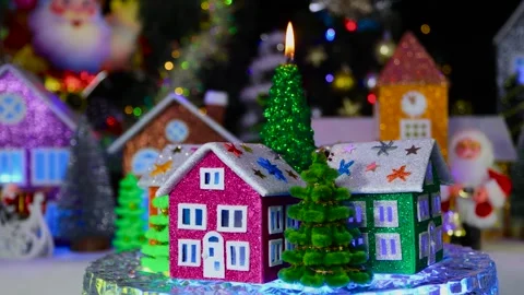 Burning candle surrounded by trees and houses rotates against of Christmas town Video stock 295758435
