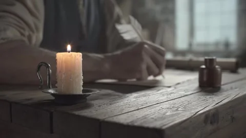 Burning candle on a table against the blurred background of a master writing Stock Footage 338991898