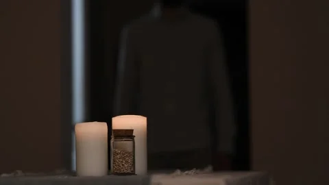 Burning candle on table as man walks by in blurred background quietly. 库存影片 309259572