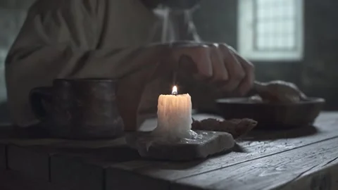 Burning candle on a table, shackled prisoner eating porridge in the background 스톡 동영상 339631200