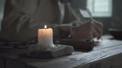 Burning candle on a table with a shackled prisoner writing behind it Stockbeeldmateriaal 342333107