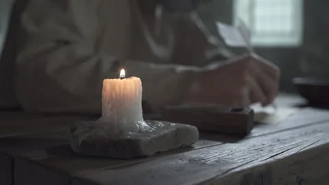 Burning candle on a wooden table with a prisoner writing in the background Stock Footage 342016595