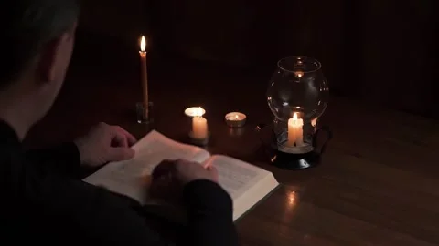 Burning candles on a table in a dark room. A man reading a book Stock Footage 310538590