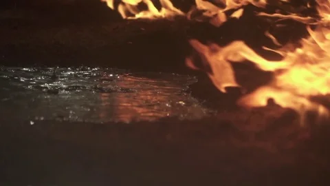 Burning fire next to a pond with water raining down as lights flicker 動画素材 76801019