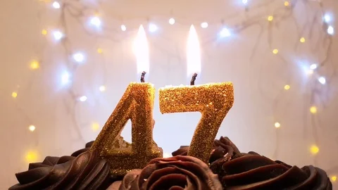 Burning gold candles in the shape of the number 47 on a birthday cake Stock Footage 105447560
