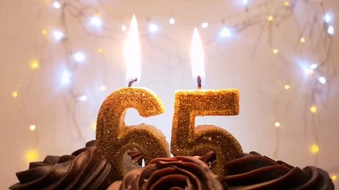 Burning gold candles in the shape of the number 65 on a birthday cake Stock Footage 105447771