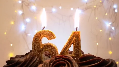 Burning gold candles in the shape of the number 64 on a birthday cake Stock Footage 105447773