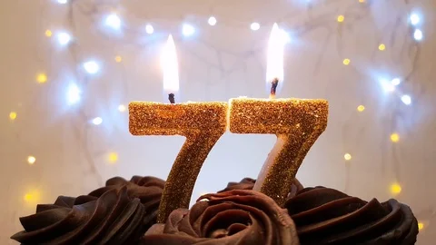 Burning gold candles in the shape of the number 77 on a birthday cake Stock Footage 105448767