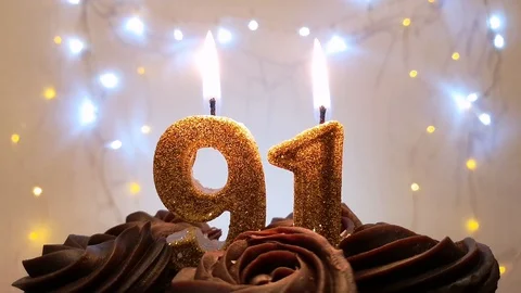 Burning gold candles in the shape of the number 91 on a birthday cake Stock Footage 105448904
