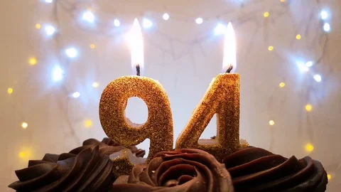 Burning gold candles in the shape of the number 94 on a birthday cake Stock Footage 105448922