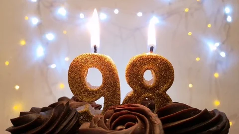 Burning gold candles in the shape of the number 98 on a birthday cake Stock Footage 105448947