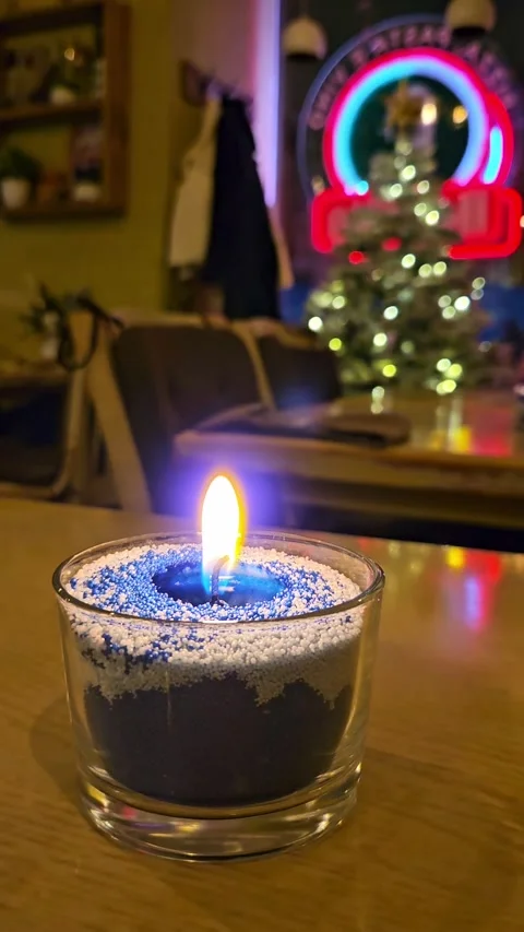 Burning granular wax candle with blurred Christmas tree and lights on background Stock Footage 346239196