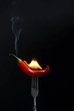 Burning hot red pepper on fork. Black background Stock Photos