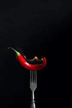Burning hot red pepper on fork. Black background Stock Photos