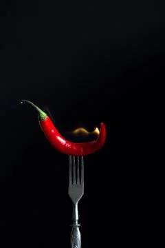 Burning hot red pepper on fork. Black background Stock Photos