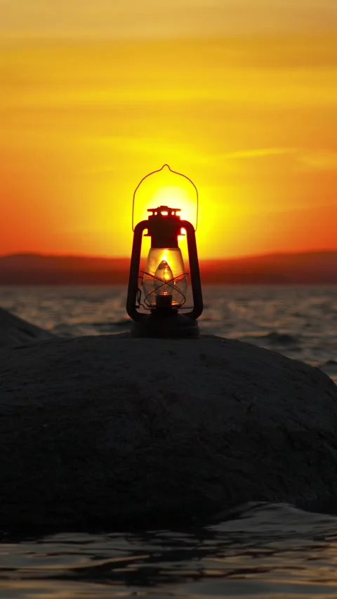 A burning lantern stands on a large stone on the shore of the lake at sunset. Видео 336620897