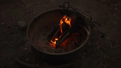 Burning logs glow with orange flames inside metal campsite fire pit Stock Footage 342303420