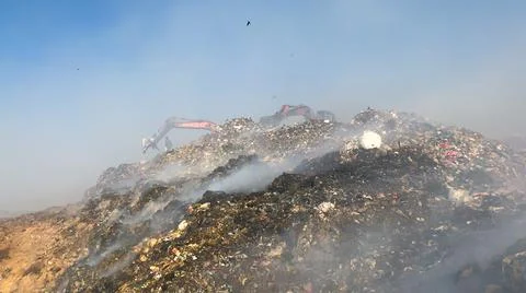 Burning pile of garbage at dump ground or landfill Excavator segregating garbage Stock-Fotos