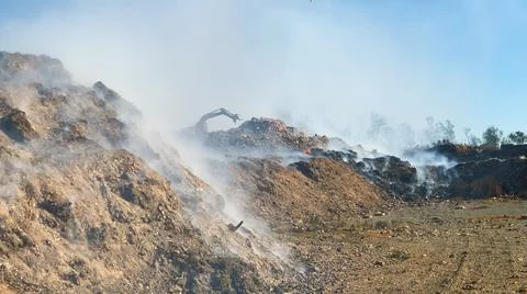 Burning pile of garbage at dump ground or landfill Excavator segregating garbage Stock-Fotos