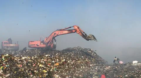 Burning pile of garbage at dump ground or landfill Excavator segregating garbage Stock-Fotos