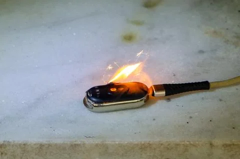 Burning smartwatch connected to cable lies on surface during device fire in.. 스톡 사진