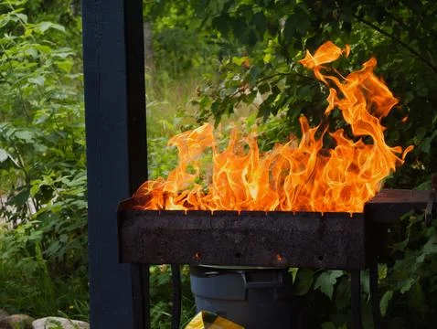 Burning wood with a bright orange flame inside a metal grill Stock Photos