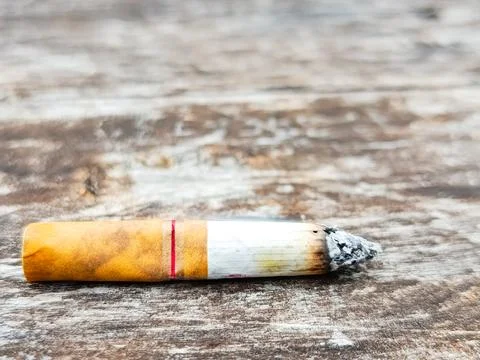 Burnt cigarette butt lying on a weathered wooden surface Stock Photos