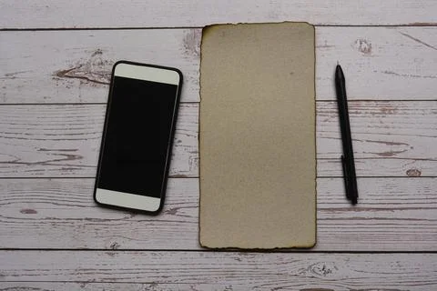 Burnt edge brown paper with pen and smartphone on wooden desk. Blank for text Stock Photos