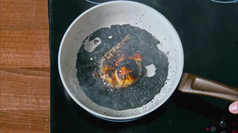 Burnt egg on a white pan in black oil on a black stove. top shot 100fps Stock Footage 196500649