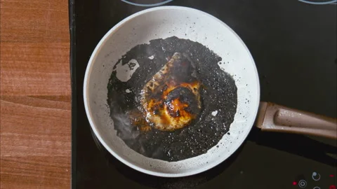 Burnt egg on a white pan in black oil on a black stove. top shot 100fps Stock Footage 196500959