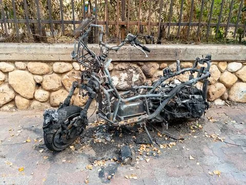 Burnt motorcycle frame after a fire on a city street. Charred metal, melted.. Stock Photos