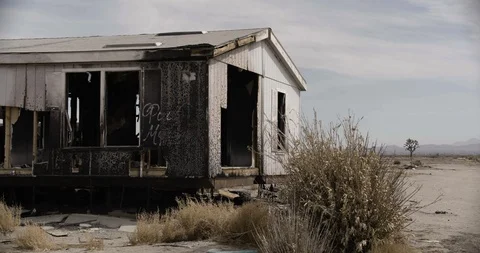 Burnt Out Trailer Home with Desert Bush in Foreground Stock Footage 89941728