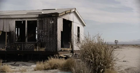 Burnt Out Trailer Home with Desert Bush in Foreground - Pan Right Stock Footage 89941733