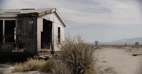Burnt Out Trailer Home with Desert Bush in Foreground - Pan Left Stock Footage 89941744