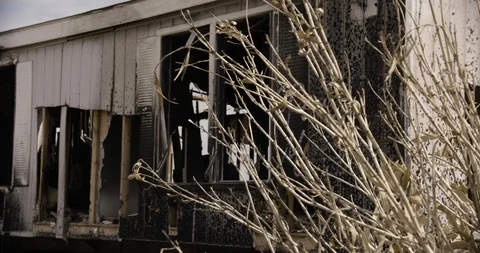 Burnt Out Trailer Home Medium Shot with Desert Bush in Foreground - Pan Right Stock Footage 89941748