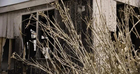 Burnt Out Trailer Home Medium Shot with Desert Bush in Foreground - Pan Left Stock Footage 89941753