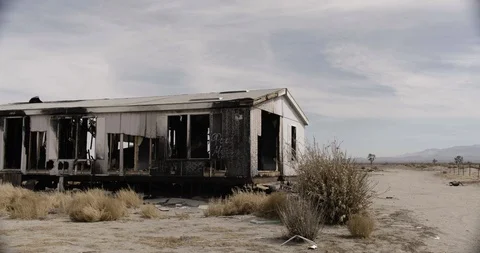 Burnt Out Trailer Home Medium Wide Shot with Desert Bush in Foreground Stock Footage 89941758