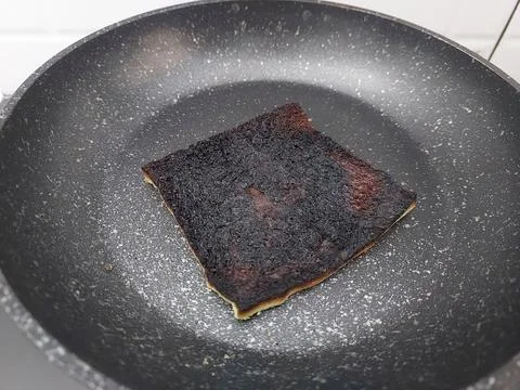 Burnt Overcooked Toast or Flatbread Charred Black in Dark Non-Stick Frying Pan Stock Photos