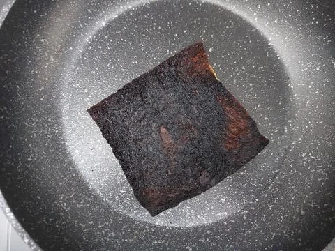 Burnt Overcooked Toast or Flatbread Charred Black in Dark Non-Stick Frying Pan Stock Photos