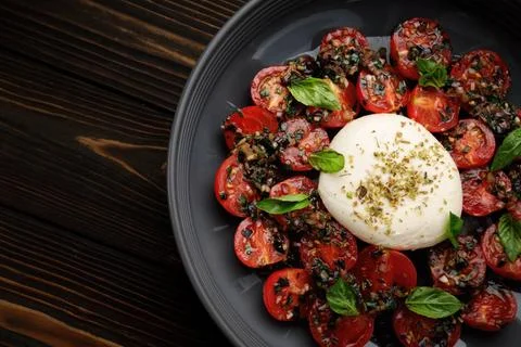 Burrata with baked cherry tomatoes and spices, on a plate, on a dark wooden.. Stock Photos