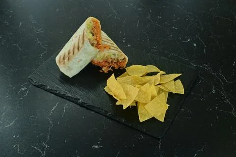 A burrito with a side of chips on a black table Stock Photos