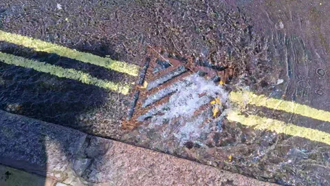 Burst water main pipe flowing down a kerbside drain. London UK, 4K. Stock Footage 341329071