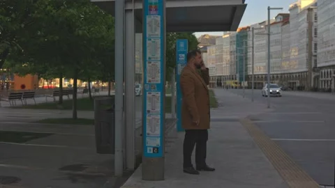 Bus stop, a man with a beard in a brown coat talking on the phone, waiting for Stock Footage 221804359