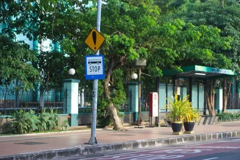 Bus stop sign on post in front of park and modern building, blue sky Stock Photos