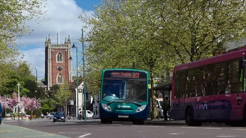 Buses drive through high street street with St Peters Church in background 스톡 동영상 74629681