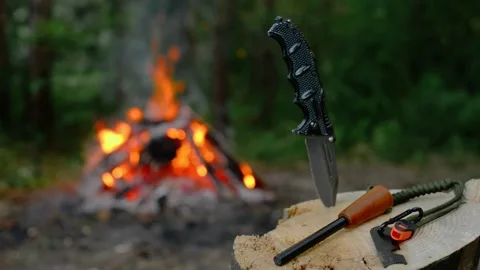Bushcraft knife and firestarter on a log with a campfire background. Stock Footage 341977836