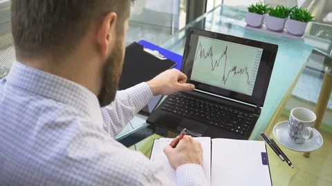 Busienessman analyzing candlestick chart on laptop computer, making notes Vidéo 73166884