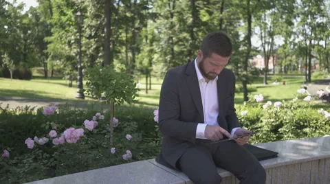 Busienessman browsing tablet  sitting on wall in park. 库存影片 52787196